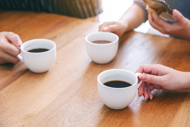 Imagen de cerca de tres personas sosteniendo tazas de café para beber en la mesa de madera - Foto, Imagen