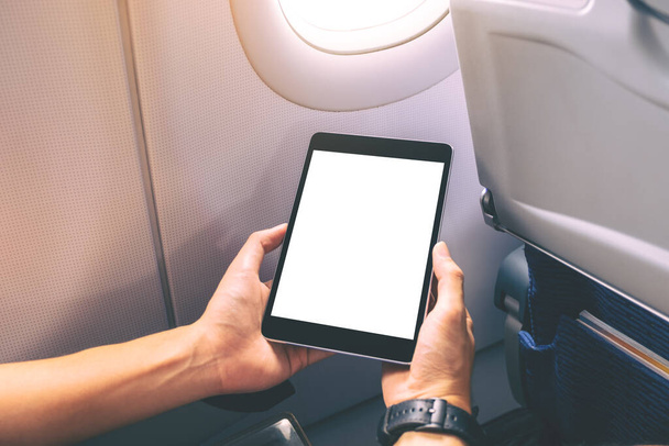 Bir uçağın penceresinin yanındaki boş beyaz masaüstü ekranlı siyah tablet bilgisayara bakan bir adamın görüntüsü. - Fotoğraf, Görsel