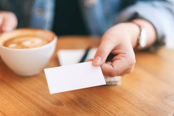 Une femme tenant et donnant une carte de visite vide vierge à quelqu'un tout en buvant du café - Photo, image