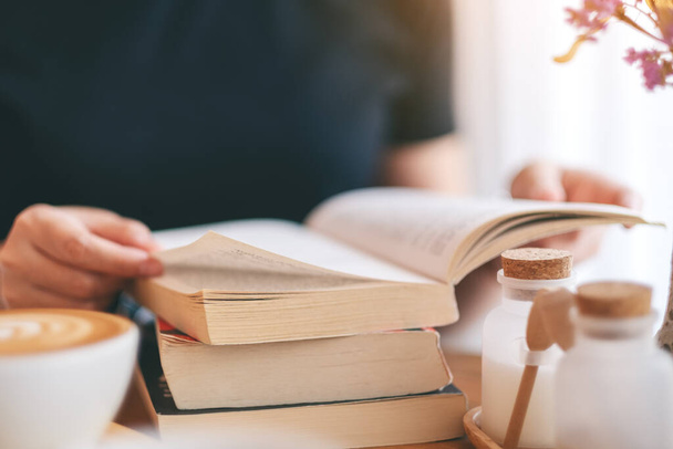 Yakından bakınca, elinde kitap tutan ve kitap okuyan bir kadının resmi. Üzerinde kahve fincanı olan ahşap bir masa. - Fotoğraf, Görsel