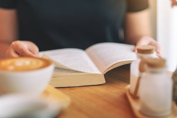 Nahaufnahme einer Frau, die ein Vintage-Buch auf einem Holztisch hält und liest - Foto, Bild