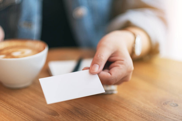 Una mujer sosteniendo y dando una tarjeta de visita vacía a alguien mientras bebe café - Foto, imagen