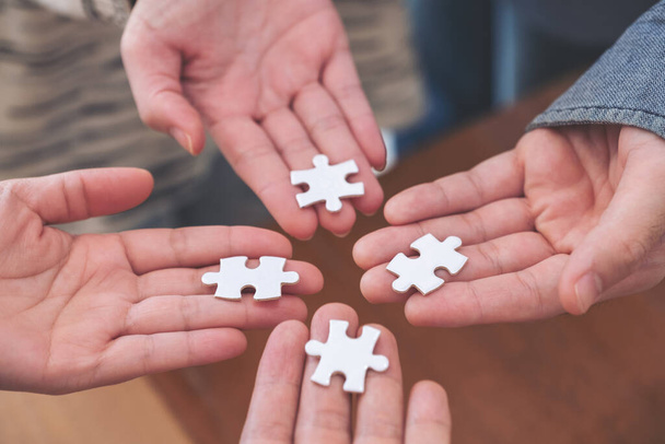 Closeup image of many people hands holding and putting a piece of white jigsaw puzzle together - Fotografie, Obrázek
