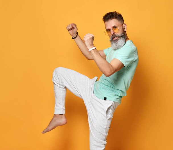 Stylish trendy gray-haired hipster guy dancing and having fun on bright orange background. - Fotoğraf, Görsel