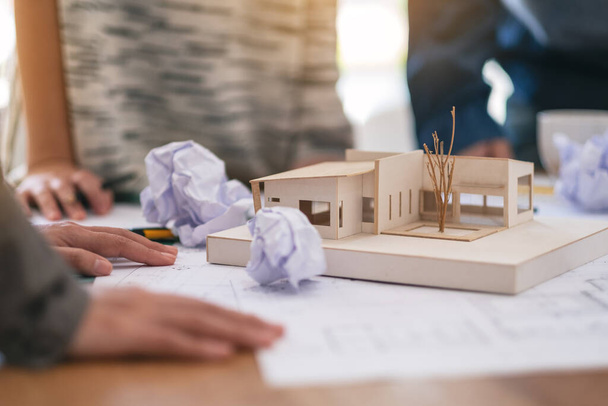 Groep van een architect mislukt tijdens het werken aan architectuurmodel en winkel tekenpapier met verknipte papieren op tafel op kantoor - Foto, afbeelding
