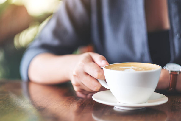 Image rapprochée d'une femme tenant et buvant du café chaud dans un café - Photo, image