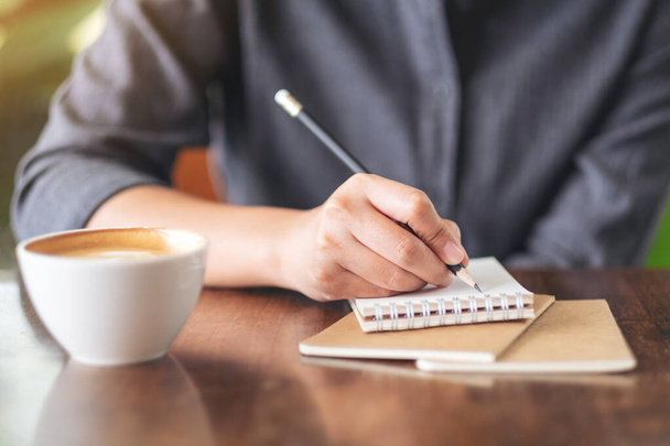 Image rapprochée d'une femme écrivant sur un carnet vierge avec une tasse de café sur la table dans un café - Photo, image