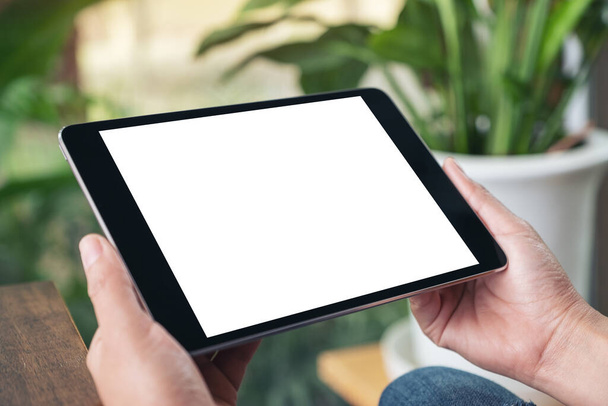 Imagen burlona de las manos sosteniendo PC tableta negra con pantalla blanca en blanco mientras está sentado en la cafetería - Foto, Imagen
