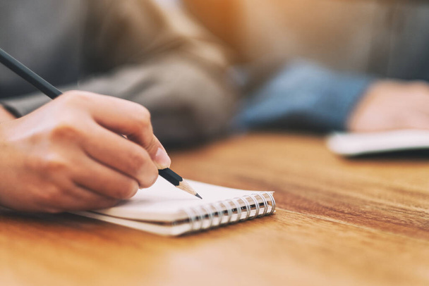 Immagine ravvicinata della mano di una donna che scrive su un quaderno bianco su un tavolo di legno - Foto, immagini