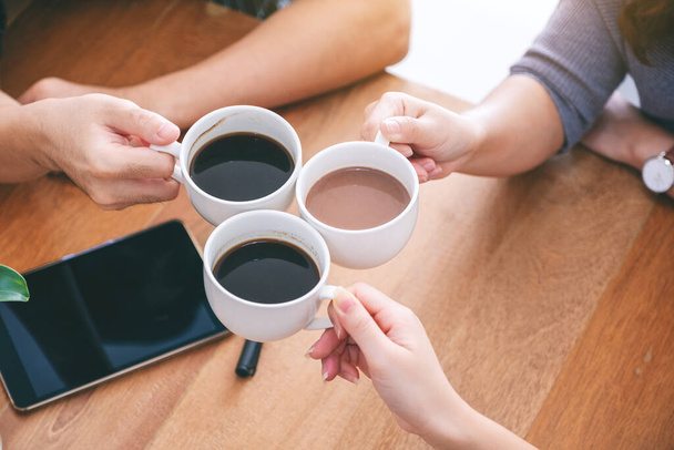 Top view image of three people clinking coffee cups on wooden table in cafe - Photo, Image