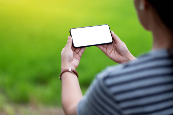 黒の携帯電話を持っている女性のモックアップイメージ黒のデスクトップ画面ととともにぼやけた緑の背景 - 写真・画像