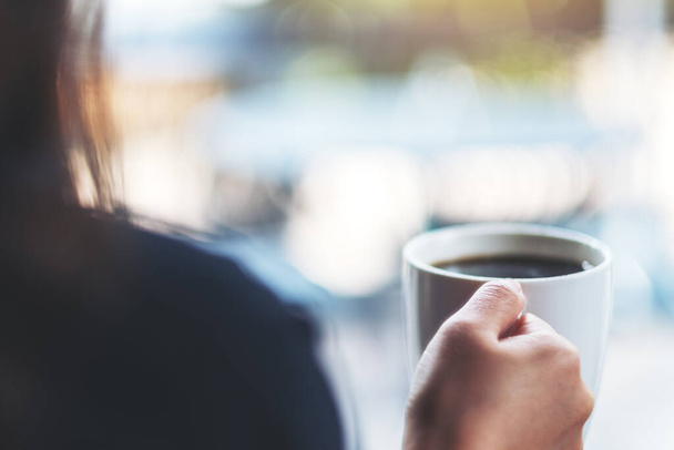 Una mujer sosteniendo una taza blanca de café caliente con fondo borroso  - Foto, imagen