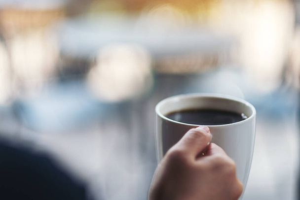 Una mujer sosteniendo una taza blanca de café caliente con fondo borroso  - Foto, imagen