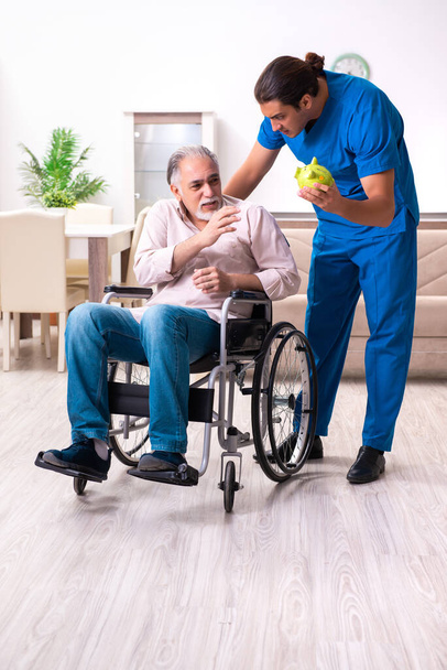 Homem velho em cadeira de rodas e jovem mau cuidador dentro de casa - Foto, Imagem