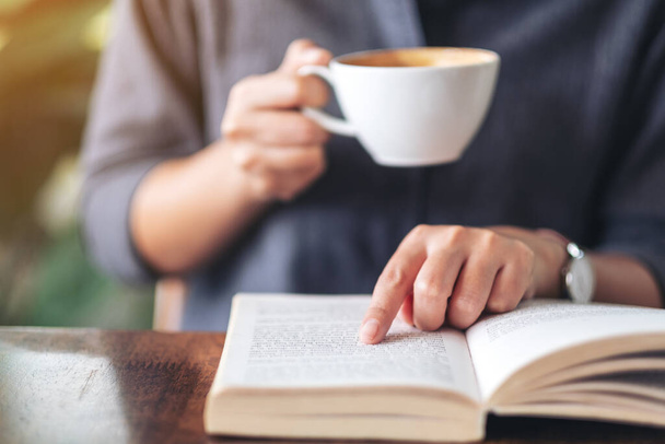 Image rapprochée d'une femme pointant et lisant un livre tout en buvant du café sur une table en bois - Photo, image