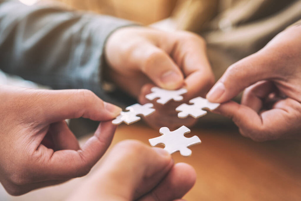 Closeup image of many people hands holding and putting a piece of white jigsaw puzzle together - Photo, Image