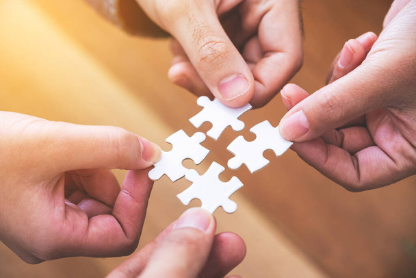 Closeup image of many people hands holding and putting a piece of white jigsaw puzzle together - Photo, Image