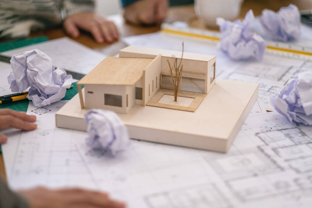 Skupina architekta se cítí vystresovaná po práci na architektonickém modelu spolu s nakresleným papírem na stole v kanceláři - Fotografie, Obrázek