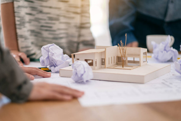 Groep van een architect voelt zich gestrest na het werken aan architectuur model samen met winkel tekenpapier op tafel in het kantoor - Foto, afbeelding
