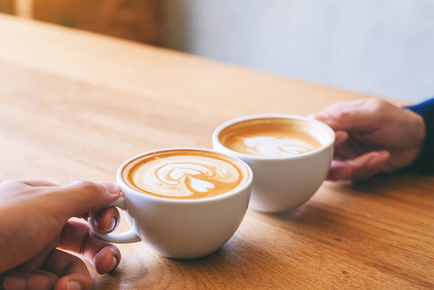 Imagen de cerca de un hombre y una mujer tintineando dos tazas de café en la mesa de madera en la cafetería - Foto, imagen
