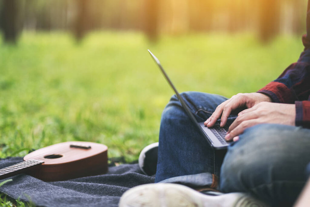 Muž pracující a píšící na klávesnici notebooku, zatímco sedí v parku - Fotografie, Obrázek