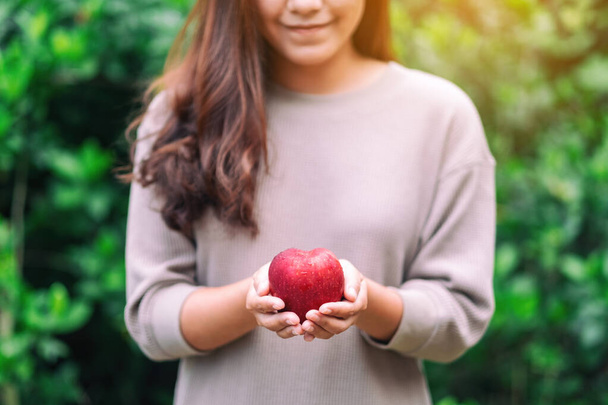 A beautiful woman holding a fresh red apple in hand - Фото, зображення
