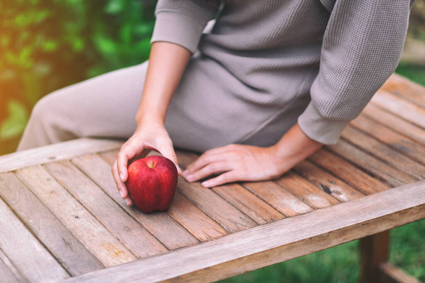 Женщина, держащая и собирающая свежее красное яблоко на деревянном столе - Фото, изображение