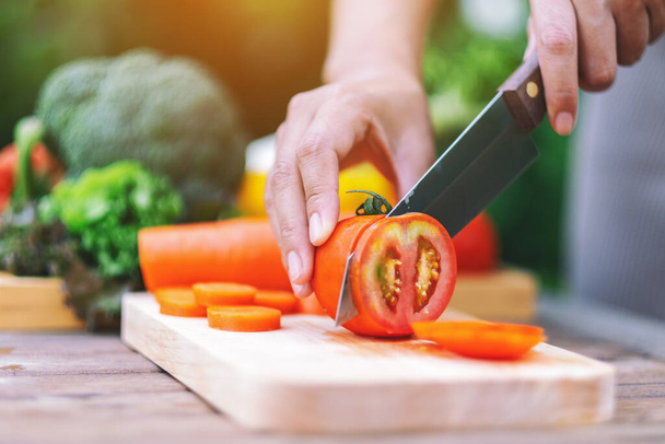 Lähikuva kuva nainen leikkaus ja pilkkominen tomaatti veitsellä puulaudalla - Valokuva, kuva