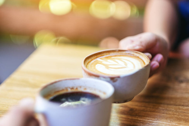 Immagine ravvicinata di due persone che afferrano tazze da caffè su un tavolo di legno  - Foto, immagini