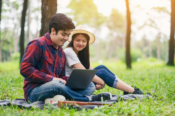 Genç bir çift parkta birlikte otururken dizüstü bilgisayara bakıp kullanıyor. - Fotoğraf, Görsel