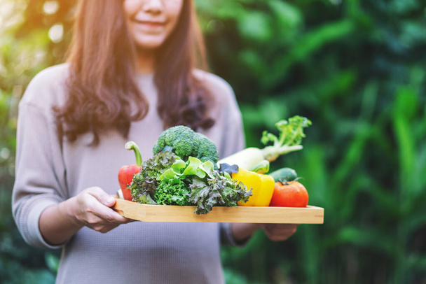 Una mujer sosteniendo una mezcla de verduras frescas en una bandeja de madera - Foto, imagen