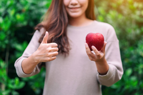新鮮な赤いリンゴに良い兆候を示すために親指を立てている女性は  - 写真・画像
