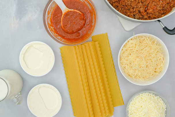 Неварені макарони лазаньї, сир в асортименті, соус маринара і мелена яловичина, інгредієнти для рецепту яловичини лазанья крупним планом на кухонному столі
 - Фото, зображення