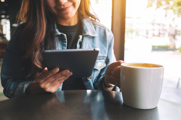 Imagen de primer plano de una mujer sosteniendo y usando la tableta PC mientras bebe café - Foto, Imagen