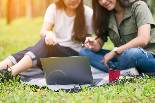 Dos mujeres asiáticas trabajando y usando computadora portátil mientras están sentadas en el parque - Foto, imagen
