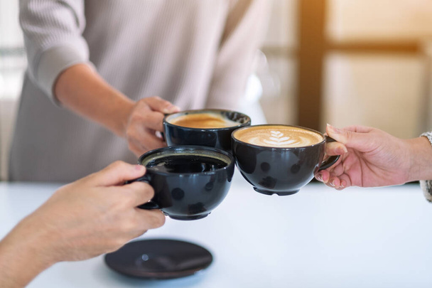Крупним планом зображення людей насолоджувалися випивкою і клінкінгом чашок кави на столі в кафе
 - Фото, зображення