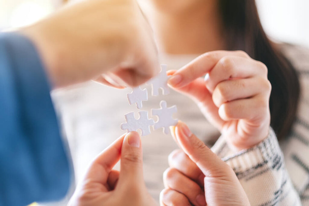 Closeup image of many people holding and putting a piece of white jigsaw puzzle together - Photo, Image