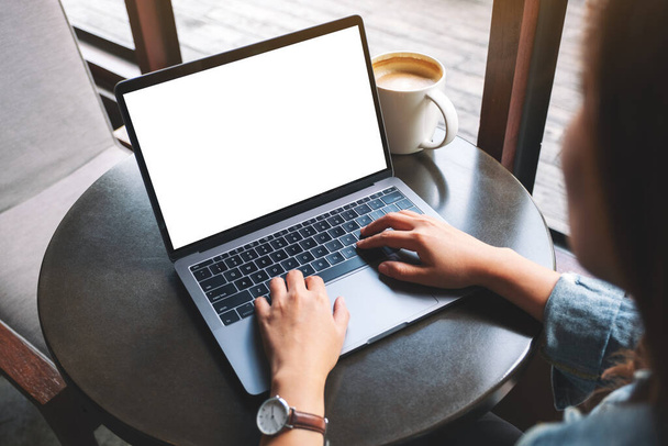 Imagem Mockup de uma woamn usando e digitando no laptop com tela de desktop branca em branco com xícara de café na mesa  - Foto, Imagem