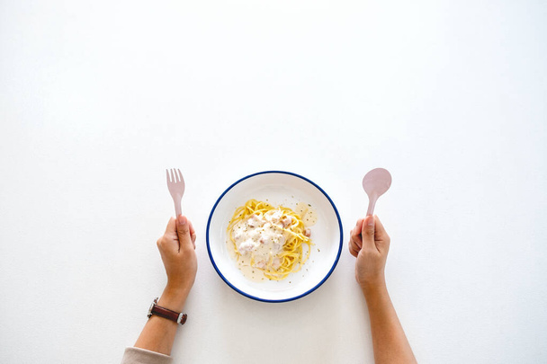 Imagem de vista superior de uma mulher segurando colher e garfo, preparando-se para comer espaguete carbonara na mesa - Foto, Imagem