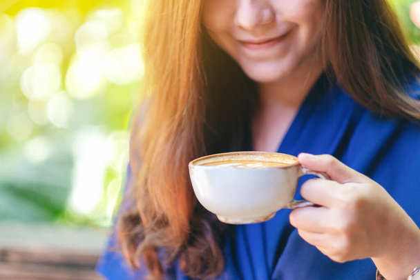 Nahaufnahme Bild einer schönen asiatischen Frau hält und trinkt heißen Kaffee im Garten - Foto, Bild