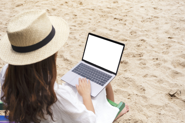 Mockup image of a woman using and typing on laptop computer with blank desktop screen while sitting on a beach chair  - Valokuva, kuva