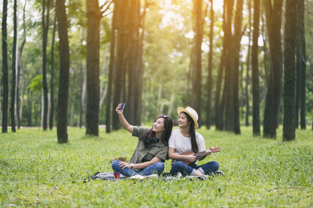Two women taking selfie while playing ukulele together in the woods - Foto, imagen