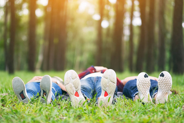 Feet of a group of young people while lying down on a green grass in the forest - Photo, image