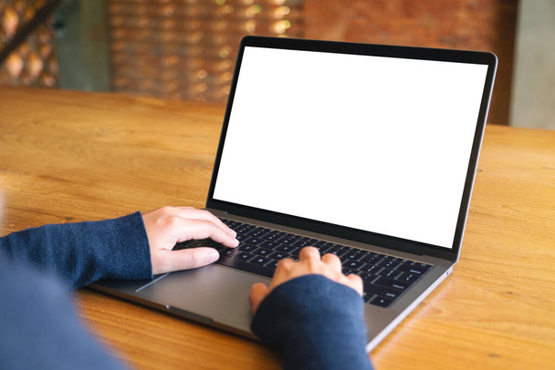 木製のテーブルの上に空白の白いデスクトップ画面とノートパソコンのキーボードを使用して入力する女性のモックアップイメージ  - 写真・画像