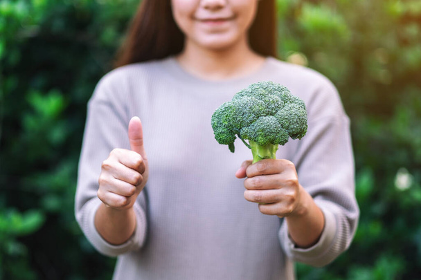 een vrouw die duim omhoog houdt en maakt om goed teken aan een groene broccoli te tonen  - Foto, afbeelding