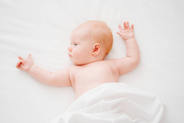 cute red-haired baby lies on a white bed. concept of baby care - Foto, immagini