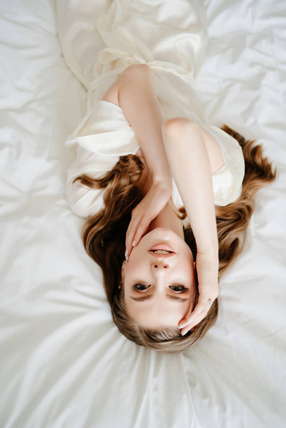 View from above.beautiful woman with makeup, long hair lies in white robe on bed - Foto, imagen