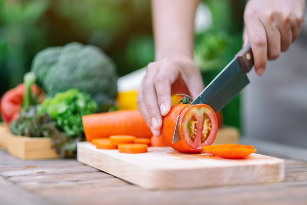 Close-up beeld van een vrouw snijden en hakken tomaat met mes op houten plank - Foto, afbeelding