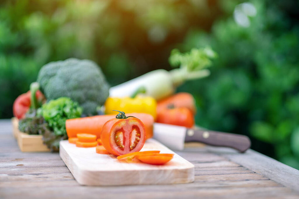 Lähikuva kuva tomaatti pilkkominen puulevy veitsellä ja lokero sekoitettu vihanneksia pöydälle - Valokuva, kuva