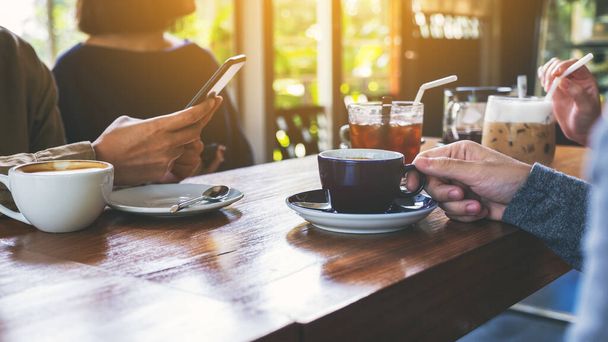 Closeup image of people using mobile phone and drinking coffee together in cafe - 写真・画像